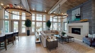 This single-story clubhouse in Panama City Beach, Florida, offers a sophisticated coastal gathering space defined by elegant architectural details and a warm, welcoming ambiance. The entrance greets visitors with soaring double-height ceilings, floor-to-ceiling windows, and light-toned tile flooring that flows seamlessly throughout the space. A grand reception area with a central table serves as the welcoming hub, adorned with decorative botanicals and community literature.

The main lounge is a showpiece, featuring dramatic wood-plank ceilings with exposed beams, large candle-style chandelier fixtures, and an expansive wall of windows that floods the room with natural light and offers views of the outdoor pool area. A contemporary fireplace with a floor-to-ceiling tile surround anchors one end of the lounge, complemented by plush sectional seating and layered area rugs.

Adjacent to the lounge is a well-appointed kitchen area showcasing a striking marble-topped island with bar seating, a decorative mosaic tile backsplash, and custom cabinetry. A separate lounge nook, finished in soft coastal blue tones with wood-ceiling accents, features curated bird artwork and intimate seating arrangements, ideal for private conversations or community gatherings. Every detail of this clubhouse reflects a refined coastal design aesthetic.