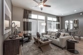 This single-story residence on E Mayo Blvd in Phoenix, Arizona, presents a thoughtfully designed open-concept floor plan with contemporary finishes and a cohesive neutral color palette. The kitchen serves as a central hub of the living area, featuring gray shaker-style cabinetry with glass-front upper cabinets, stainless steel appliances including a gas range, built-in microwave, and French door refrigerator, plus a large island with white quartz countertops, an undermount sink with a high-arc faucet, and seating for multiple guests. Brushed nickel pendant lights illuminate the island, complementing the light hardwood flooring that flows into the open dining and living areas. The living room offers generous natural light through a bank of large windows, with a ceiling fan overhead and ample space for relaxed seating arrangements. Multiple bedrooms provide comfortable retreats, each with plush carpet, ceiling fans, and natural light. The bathrooms are finished with tile flooring, shaker-style vanities with white countertops, and large mirrors. One bathroom features a dual-sink vanity with a separate shower, while another includes a soaking tub and walk-in closet access, adding functional versatility to the overall layout.