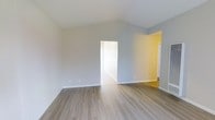 This 1-bedroom, 1-bathroom single-floor residence offers a clean and modern living environment designed for comfort and functionality. The main living area is immediately welcoming, featuring light-toned hardwood-style flooring that runs throughout the space, lending warmth and a sense of cohesion to the layout. Notably tall, vaulted ceilings amplify the sense of openness and airiness, making the space feel generously proportioned. The walls are finished in a soft, neutral gray tone that pairs seamlessly with the bright white trim and baseboards, creating a crisp and contemporary look. Natural light flows freely through the space, enhancing the light color palette and contributing to an inviting atmosphere. An open doorway connects the living area to an adjacent room with warm yellow-toned walls, adding a subtle pop of color and visual interest. The bedroom is accessed through a clean-lined doorway and continues the same light flooring and neutral finishes seen throughout. The overall design is thoughtfully understated, providing a versatile backdrop that accommodates a wide range of interior styles. This well-maintained residence is move-in ready and presents a bright, airy, and functional layout ideal for comfortable everyday living.