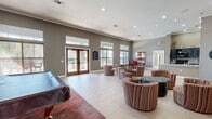 This single-floor clubhouse offers a thoughtfully designed layout that combines functionality and comfort across a generously sized open floor plan. The main living and lounge area features high ceilings with crown molding, recessed lighting, and large windows topped with transom panes that flood the space with natural light. Warm taupe and bold red accent walls create a vibrant yet welcoming ambiance, complemented by light tile flooring throughout. A variety of seating arrangements, including patterned swivel chairs and a tufted ottoman, provide flexible gathering spaces for residents.

The kitchen is equipped with dark distressed cabinetry, black appliances including a range, microwave, and refrigerator, and a spacious countertop peninsula with a sink — ideal for communal use. Adjacent to the kitchen, a dining area with large windows overlooks the outdoor pool, offering a bright and inviting setting for casual meals.

A dedicated billiards room adds a recreational dimension to the space, featuring soaring ceilings, a full-size pool table, and oversized windows that bring in ample daylight. Decorative wall panels and a high-top seating arrangement complete this entertaining area. Elegant wood-framed French doors lead directly to the outdoor pool area, seamlessly connecting the interior to the exterior amenities.