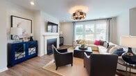 Located at 503 Merrion Park Ln in Morrisville, NC, this thoughtfully designed three-story home offers a harmonious blend of modern style and functional living across multiple levels. Hardwood flooring flows throughout the main living areas, anchored by a staircase with rich wood treads and crisp white risers. The main level showcases an open-concept layout where the kitchen, dining, and living areas connect seamlessly. The kitchen is outfitted with soft gray cabinetry, dark stone countertops, stainless steel appliances, and a central island with bar seating, with direct access to an outdoor deck. The adjacent dining area features a striking orb chandelier and large windows that invite natural light. A lower-level living room impresses with a bold navy accent wall, a statement sputnik chandelier, and French doors opening to the outdoors. Upstairs, a spacious lounge area offers large windows and an eye-catching geometric ceiling fixture. The primary bedroom features a tray ceiling, shiplap accent wall, plush carpet, and generous natural light. Its en-suite bath includes a dual-sink vanity with white cabinetry and marble-style tile flooring. A large walk-in closet with built-in shelving and a natural light window completes the primary suite. Throughout, the home balances refined finishes with a warm, livable character.
