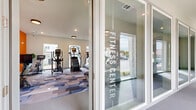 The Gibson Fitness Center is a thoughtfully designed, single-floor facility that offers a comprehensive workout environment for residents. Upon entry, glass-paneled doors etched with "Fitness Center" provide a welcoming and professional introduction to the space. The interior is defined by a vibrant, geometric patterned carpet in shades of blue, grey, and lavender, which adds energy and visual interest throughout.

A striking orange accent wall branded with "The Gibson" logo serves as a bold focal point, lending the space a modern, motivating atmosphere. Recessed and flush-mounted ceiling lights ensure the room is well-lit, while large windows along multiple walls invite abundant natural light and offer views of the surrounding community.

The cardio zone is generously equipped with multiple treadmills, elliptical trainers, a rowing machine, and stair climbers, providing a full range of aerobic training options. The strength area features a multi-functional cable machine, adjustable benches, and a well-stocked dumbbell rack. An expansive floor-to-ceiling mirror visually enlarges the space and supports proper form during workouts.

The overall ambiance is clean, contemporary, and energizing, combining functional fitness amenities with a polished aesthetic that reflects the character of The Gibson community.