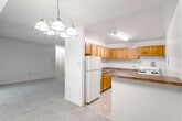 This single-floor residence offers a functional and straightforward layout with well-defined living spaces throughout. The kitchen is equipped with warm honey-toned wood cabinetry spanning both upper and lower sections, providing generous storage. Dark laminate countertops wrap around the workspace in an L-shape, accompanied by a stainless steel double sink and a white refrigerator. The kitchen opens to a dining area via a raised breakfast bar, overhead which hangs a multi-arm chandelier that adds a classic touch to the space.

The living area is carpeted and bathed in natural light from a large sliding glass door that opens to a private balcony overlooking lush greenery. The open connection between the living and dining areas creates a spacious, cohesive feel. Bedrooms are carpeted and neutrally toned, each offering ample space and closet storage with bifold doors. One bedroom benefits from a window with outdoor views.

The unit includes two bathrooms: one featuring a tub-shower combination with a white surround, a single vanity with wood cabinetry, and a medicine cabinet mirror; the other offering a standalone walk-in shower, toilet, and vanity. Tile flooring runs through both bathrooms, while neutral carpet covers the remaining living spaces, contributing to a consistent, understated aesthetic throughout.