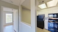 This single-floor unit offers a functional and comfortable layout designed with practical living in mind. The kitchen is a standout feature, equipped with black appliances including a refrigerator, electric range, and over-the-range microwave, all complemented by crisp white cabinetry, light stone countertops, and a classic subway tile backsplash. A skylight and window bring natural light into the cooking space, while a stainless steel double sink adds to its utility. A pass-through cutout connects the kitchen area to the hallway, enhancing the sense of openness throughout. The living area impresses with vaulted ceilings and a large sliding glass door fitted with vertical blinds, allowing abundant natural light and outdoor views to fill the room. Light wood-style flooring runs consistently throughout the unit, tying the spaces together with a clean, cohesive aesthetic. The bedroom is generously sized, featuring two windows on adjacent walls, a ceiling fan with integrated lighting, and the same warm flooring. The bathroom includes a vanity with stone countertops, white cabinetry, a large mirror, and a separate tub-shower combination. Neutral gray walls and textured ceilings complete the understated, move-in-ready character of this well-maintained space.