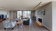 Located in the heart of Minneapolis, this high-rise residence offers an impressive living experience defined by sweeping city skyline views and thoughtfully designed interiors. The open-concept living room is anchored by hardwood-style flooring, a sleek track lighting system, and a contemporary fireplace, while expansive floor-to-ceiling windows and sliding glass doors flood the space with natural light and frame dramatic views of the downtown skyline. The dining area flows seamlessly from the living room and features a glass-top table beneath a modern chandelier, with track lighting extending throughout. The kitchen is outfitted with white cabinetry, granite countertops, a distinctive stainless steel farmhouse sink, mosaic tile backsplash, and stainless steel appliances. Multiple bedrooms provide comfortable retreats, with soft carpeting, generous closet space, and large windows showcasing city and neighborhood panoramas. The primary bedroom benefits from direct balcony access and wide skyline views. Bathrooms are finished with granite-topped vanities, chrome fixtures, and clean white tile. The overall palette of cool grays and warm wood tones creates a cohesive, contemporary urban ambiance throughout this well-appointed Minneapolis residence.