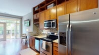 Located at 600 St. Mary's St in the heart of Raleigh, NC, this single-floor residence combines modern finishes with a warm, inviting atmosphere throughout. Rich hardwood flooring flows consistently across the living, sleeping, and transitional spaces, creating a cohesive and polished aesthetic.

The kitchen is well-appointed with warm-toned wood cabinetry extending to the ceiling, offering generous storage including open display shelving and a built-in wine rack. A mosaic tile backsplash adds visual texture, while stainless steel appliances — including a side-by-side refrigerator with ice and water dispenser, electric range, over-the-range microwave, and dishwasher — provide a fully equipped cooking experience with light stone countertops completing the look.

The living area is bright and open, benefiting from large sliding glass doors that lead to a private balcony, filling the space with natural light and offering outdoor views. The bedroom is generously proportioned with ample floor space, a built-in nook with shelving, and a relaxed, comfortable ambiance suited for both rest and everyday living.

The bathroom features neutral tile flooring, a walk-in tiled shower with glass enclosure, a wood-toned vanity with stone countertop, and a louvered closet door, offering a clean and functional design. Track lighting in the hallway adds a modern touch to the overall layout.