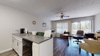 This single-floor space is thoughtfully laid out to serve as a functional management office, combining practical work areas with residential-style amenities. The open-plan main area seamlessly connects the kitchen to the primary office workspace, creating an efficient and accessible environment. A ceiling fan overhead and a large window with horizontal blinds allow for natural light and comfortable airflow throughout the space.

The kitchen is well-equipped with white cabinetry, gray speckled countertops, and a full suite of black appliances including a range, over-the-range microwave, and refrigerator. The galley-style layout maximizes use of the available space while maintaining a clean, organized appearance.

The main office area features a large executive desk, seating for visitors, and a dedicated reception counter, making it well-suited for administrative operations and client interactions. Crown molding adds a subtle decorative detail, while a ceiling fan contributes to the room's functionality.

The full bathroom is cleanly appointed with a white vanity, gray countertop, a combination tub and shower with a decorative curtain, and safety grab bars — reflecting accessible design considerations. Throughout the space, wood-look plank flooring provides a cohesive, durable, and attractive finish that ties all areas together. The textured ceilings and neutral wall tones complete the practical, professional character of this well-maintained unit.