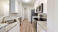 This single-floor residence at Greenfield Crossing in Greenfield, Indiana offers a well-appointed layout with contemporary finishes throughout. The kitchen serves as a central highlight, showcasing white shaker cabinetry, granite countertops with striking veining, and a full suite of stainless steel appliances including a range, microwave, refrigerator, and dishwasher. A curved breakfast bar extends into the living area, creating a natural transition between spaces. Wood-look luxury vinyl flooring runs through the kitchen and utility areas, while plush carpeting covers the living room and bedrooms.

The living room is generously sized, featuring vaulted ceilings, a fireplace with a sleek surround, and French doors that open to a private balcony with outdoor views. Bedrooms are well-proportioned, offering natural light through blinds-equipped windows and sliding or hinged closet doors for ample storage.

The bathrooms are finished with white shaker vanities, brushed nickel hardware, and wood-look vinyl flooring. A dedicated laundry room includes washer/dryer hookups, a built-in shelf, and gas and electric connections. The overall aesthetic is clean and modern, with neutral tones creating a cohesive, move-in-ready atmosphere throughout.