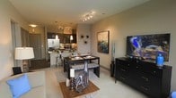 This thoughtfully designed single-floor residence showcases an open-concept floor plan that effortlessly integrates the living, dining, and kitchen spaces into one cohesive and inviting environment. The kitchen is a standout feature, outfitted with dark cabinetry, stainless steel appliances, a mosaic tile backsplash, and a breakfast bar with pendant lighting that adds a warm, contemporary touch. Track lighting overhead ensures the space is well-lit and functional. The dining area comfortably accommodates a full dining table and bench seating, making it ideal for both casual meals and entertaining. Flowing seamlessly from the dining space, the living area provides a relaxed atmosphere with soft, neutral-toned walls and plush carpeting that adds warmth underfoot. Curated décor elements, including wall art and sculptural accents, lend the space a polished, modern aesthetic. The overall ambiance is warm and sophisticated, with a neutral color palette of tans and deep espresso tones creating a harmonious and inviting atmosphere throughout. The seamless flow between each zone makes this residence feel both spacious and efficiently connected.