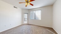 This single-floor home offers a practical and comfortable layout across five bedrooms and two full bathrooms. The open-concept kitchen and living room serve as the heart of the home, featuring an L-shaped kitchen with warm wood cabinetry, granite-style countertops, stainless steel appliances including a refrigerator, microwave, and electric range, and a peninsula with pendant lighting overhead. Tile flooring anchors the kitchen area, while plush carpet extends into the living space. Each of the five bedrooms is carpeted and bathed in natural light through large windows fitted with vertical blinds. Ceiling fans are present throughout, providing year-round comfort. The spacious primary bedroom includes direct outdoor access via a glass-paned door. A walk-in closet with built-in shelving and hanging rods offers generous storage. The two bathrooms are finished with tile flooring, warm wood vanities with dark countertops, and tub-shower combinations accented by decorative tile surrounds and natural light from overhead windows. A central hallway connects the rooms efficiently. The home's clean, neutral palette and consistent finishes create a cohesive and welcoming atmosphere throughout.
