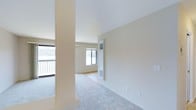 This single-floor residence offers two bedrooms and two bathrooms within a well-proportioned, open layout. The interior is finished in a clean, neutral palette of soft whites and warm beige tones, creating a bright and welcoming atmosphere throughout. Light-colored carpeting flows across the main living areas, contributing to a cohesive and understated design.

The living area is defined by a structural column that subtly delineates the space while preserving an open feel. A wall-mounted heating and cooling unit provides climate control, and multiple windows allow generous natural light to fill the room, enhancing the sense of spaciousness. Sliding glass doors open to a private balcony or patio, offering outdoor access and additional light.

The layout transitions smoothly from the living area toward the interior rooms, with wide openings and a consistent design language tying the spaces together. The smooth, high ceilings further amplify the airy quality of the home.

Overall, this residence presents a straightforward, functional design with clean finishes, ample natural light, and practical features, making it a comfortable and well-appointed living space suited for everyday living.