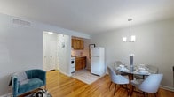 This single-floor residence at The Gardens at Raritan offers a cohesive, well-organized layout designed for comfortable everyday living. Warm hardwood flooring flows throughout the main living areas, lending a consistent and inviting character to the space.

The living room provides a comfortable gathering area with light gray walls, a geometric-patterned area rug, and ample wall space suited for artwork. It transitions naturally into a dedicated dining area, which is anchored by a modern chandelier and a window that brings in natural light. A glass-top round dining table with upholstered chairs occupies this space efficiently.

The kitchen is positioned adjacent to the dining area and features warm oak cabinetry, a tile backsplash, a gas range, a full-size refrigerator, and a stainless steel sink — offering practical functionality in a compact footprint.

The bedroom is a calm, light-filled retreat with soft gray walls, hardwood flooring, a ceiling fan with lighting, and a window with outdoor views framed by neutral curtains.

A hallway connects the main areas, with access to the full bathroom. The bathroom features tile surround walls with a decorative mosaic accent border, a soaking tub with shower, and a vanity with chrome fixtures.