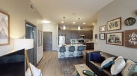 This single-floor unit showcases a thoughtfully designed open-concept layout that seamlessly connects the living, dining, and kitchen areas. The kitchen is a standout feature, outfitted with dark espresso cabinetry extending to the ceiling, granite countertops, and stainless steel appliances including a refrigerator, microwave, and range. A peninsula with seating for three provides a casual dining option, while pendant lighting adds a contemporary touch overhead. Recessed lighting and elevated ceilings contribute to an airy, open feel throughout the common area.

The living room is well-proportioned, with wood-style flooring, a ceiling fan, and a large window with access to an outdoor area, allowing ample natural light to fill the space. Multiple bedrooms offer comfortable accommodations, each with windows providing natural light and views of the surrounding area. The bedrooms include space for a desk, making them functional for work or study.

The bathrooms are finished with granite-topped dark vanities, large mirrors, and tile flooring. One bathroom features a shower-tub combination, while another includes a spacious vanity with generous counter space. The overall design palette of neutral grays, dark accents, and warm wood tones creates a cohesive and modern ambiance throughout.