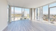 Located on the 10th floor at 492 W 41st Ave in Vancouver's Cambie corridor, this 2-bedroom, 1-bathroom unit offers a thoughtfully designed open-concept layout with modern finishes throughout. Light wood-tone laminate flooring runs seamlessly across the entire unit, complementing the bright, neutral palette.

The combined kitchen and living area forms the heart of the unit. The kitchen is outfitted with flat-panel white cabinetry extending to the ceiling, quartz countertops, a marble-style tile backsplash, stainless steel appliances including a built-in oven, microwave, dishwasher, and refrigerator, and recessed pot lighting. The living area benefits from expansive floor-to-ceiling windows and access to a private balcony, framing sweeping panoramic views of the Vancouver cityscape and surrounding neighbourhoods.

Both bedrooms feature large windows that capture abundant natural light and elevated city views, with warm-toned laminate flooring and clean, neutral walls. The primary bedroom includes generous proportions and direct access to natural light.

The bathroom is finished with polished porcelain tile flooring, a glass-enclosed standing shower with full marble-style tile surround, a wall-mounted vanity with under-mount sink, and recessed lighting. A dedicated closet provides additional storage. The unit's elevated position and wall-to-wall glazing make natural light and city views defining features throughout.