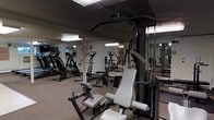 Located at 800 Kimberton Road in Phoenixville, Pennsylvania, this fitness center offers a dedicated space for exercise and wellness on a single floor. The gym is equipped with a diverse selection of workout machines designed to support both cardiovascular and strength training routines. Cardio equipment includes treadmills and elliptical-style machines, providing options for aerobic exercise. The strength training area features a multi-functional cable and pulley machine with adjustable attachments, along with additional weight and resistance equipment to accommodate a range of exercises. Large mirrors line the walls, creating a sense of expanded space while allowing users to monitor their form during workouts. The flooring is fitted with durable, cushioned material suited for a gym environment. Overhead fluorescent lighting ensures the space is well-lit throughout. The layout is practical and functional, with equipment arranged to allow comfortable movement between stations. Overall, the fitness center provides a well-equipped, no-frills environment focused on delivering a comprehensive workout experience.