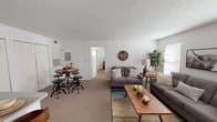 This single-story unit offers a well-organized layout designed for comfortable everyday living. The main living area is generously proportioned, featuring wall-to-wall carpet, textured ceilings, and multiple windows fitted with blinds that allow natural light to fill the space. The living room accommodates a full seating arrangement and includes a dedicated dining nook, providing a versatile space for both relaxing and entertaining. A wall-mounted electrical panel and a built-in heating unit are also present, adding functional utility to the area.

The kitchen is efficiently designed with light wood cabinetry, ample counter space, a gas range with overhead ventilation, a stainless steel sink, and wood-look flooring. Storage is well distributed through upper and lower cabinet configurations.

The unit includes two bedrooms, each carpeted and finished with neutral walls and windows that bring in natural light. The primary bedroom is notably spacious, offering room for a full bedroom suite with multiple windows providing additional brightness.

The bathroom features wood-look flooring, a single-sink vanity with a large mirror, a tub-and-shower combination with a decorative curtain, and a ceiling ventilation fan. Overall, the unit presents a clean, neutral palette suitable for a variety of interior styles.