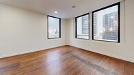 Located in the heart of downtown Tulsa, this thoughtfully designed one-bedroom, one-bathroom residence offers a compelling blend of modern finishes and urban convenience. The open-concept kitchen and living area serves as the centerpiece of the home, showcasing rich hardwood floors, a sleek kitchen island with white quartz countertops, two-tone cabinetry with white upper and dark espresso lower cabinets, a tile backsplash, and stainless steel appliances. Contemporary loop pendant lighting adds a striking design element above the island. Large, black-framed windows fill the living area with natural light and frame impressive views of the downtown Tulsa skyline. The bedroom features light tile flooring, a ceiling fan, and a generous window that continues the urban views, while an adjacent closet provides ample storage. The bathroom is finished to a high standard, with dark marble-style tile flooring, a glass-enclosed walk-in shower with coordinating tile surround, a white vanity with a stone countertop, and gold-accented fixtures. Clean white walls and recessed lighting throughout the unit contribute to a bright, cohesive, and polished atmosphere well-suited for downtown living.
