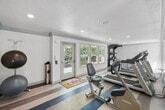 Located at 240 Burt St in Santa Rosa, California, this fitness center offers a comprehensive exercise facility designed to support a range of workout routines. The single-floor gym features a distinctive striped wood-look flooring in neutral and blue tones, lending the space a clean, modern aesthetic that complements its bright white walls and crown molding details.

The cardio zone is well-stocked with multiple treadmills, elliptical trainers, and stationary bikes, all arranged to maximize use of the available floor space. A floor-to-ceiling mirrored wall runs along one side of the main exercise area, visually expanding the room while allowing users to monitor their form during workouts. Recessed lighting throughout ensures consistent illumination across the entire space.

A dedicated strength training area includes a multi-functional cable machine and an adjustable workout bench, providing options for resistance and weight training. A dumbbell rack with a full range of free weights adds further versatility. Storage cabinetry is also present, keeping the space organized and functional.

Large windows invite generous natural light and offer views of the surrounding greenery and outdoor pool area. A direct exterior door provides convenient access to the pool deck, connecting indoor and outdoor fitness and recreation areas seamlessly.