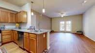 This single-floor residence offers a well-designed, open-concept layout that seamlessly connects the kitchen and living areas. The kitchen is a standout feature, equipped with warm honey-toned wood cabinetry, granite-style countertops, a full suite of stainless steel appliances including a refrigerator, gas range, and microwave, and a peninsula island with a double basin sink and elegant pendant lighting overhead. The open living area flows naturally from the kitchen, featuring durable hardwood-style flooring, a ceiling fan, and a set of glass French doors that invite natural light and provide access to the outdoors.

The bedrooms are generously proportioned, each finished with the same warm hardwood-style flooring, ceiling fans, and large windows fitted with blinds that offer both natural light and privacy. One bedroom benefits from multiple windows on adjacent walls, enhancing its bright, airy feel.

A secondary room features a ceiling fan and additional track lighting alongside French door access, offering flexible use as a living or flex space. The primary bathroom is notably spacious, boasting an extended dual-sink vanity with warm wood cabinetry, large mirrors, and a glass-enclosed shower. A secondary bathroom provides a clean, functional toilet area also finished with hardwood-style flooring. Neutral, warm tones are consistent throughout, giving the entire residence a cohesive and inviting ambiance.