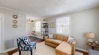 Located at 614 Peninsula Dr in Newport News, VA, this efficiently designed single-floor, one-bedroom, one-bathroom home makes excellent use of its compact footprint. The living room serves as the heart of the space, featuring rich hardwood flooring, crown molding, and a textured ceiling throughout. Multiple large windows with white blinds flood the room with natural light, creating a bright and welcoming atmosphere. A ceiling fan adds comfort, while an adjacent dining nook provides a functional space for everyday meals. The bedroom offers a quiet retreat, complete with hardwood floors, crown molding, a textured ceiling, and a window that allows natural light to filter in — providing a calm and restful environment. The full bathroom is clean and straightforward, featuring a white tiled tub-shower combination. A dedicated laundry area houses the water heater and utility connections, with overhead shelving for added storage. Neutral gray wall tones and white trim throughout the home create a cohesive, understated aesthetic. The overall ambiance is cozy and practical, well-suited for those seeking low-maintenance, single-level living in Newport News.