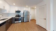 This contemporary single-floor residence offers a thoughtfully designed layout with clean lines and modern finishes throughout. The kitchen serves as a standout feature, boasting white upper cabinetry paired with dark wood-toned lower cabinets, crisp white quartz countertops, a subtle tile backsplash, and a full suite of stainless steel appliances including a gas range, microwave, dishwasher, and refrigerator. Warm-toned hardwood-style flooring runs through the kitchen and living areas, creating a cohesive and inviting atmosphere.

The open living area is bright and airy, featuring track lighting and a sliding glass door that leads to a private outdoor space, allowing natural light to fill the room. The layout flows seamlessly from the living space into the kitchen, making it ideal for everyday living and entertaining.

The bedrooms are comfortably sized and finished with soft wall-to-wall carpeting and windows that bring in natural light. The bathroom is elegantly appointed with a floating dark wood vanity, a backlit mirror, white countertop, large-format tile flooring, and a glass-enclosed soaking tub and shower combination. A louvered closet door adds a functional and stylish touch near the entryway, completing this well-designed modern residence.