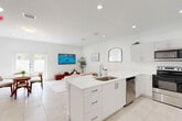 Located at 3031 NW Sixth St in Pompano Beach, FL, this two-story home offers a clean, modern aesthetic defined by crisp white walls, recessed lighting, and light-toned tile flooring throughout. The ground floor houses the main living spaces, including an open-plan living room, dining area, and kitchen. The kitchen is outfitted with white shaker cabinetry, light quartz countertops, a central island with sink, and a full suite of stainless steel appliances. The dining area adjoins the kitchen and benefits from natural light through a window overlooking the outdoor space. The living room is bright and airy, opening toward a balcony. A garage and entrance area complete the lower level. The upper floor contains two bedrooms, three bathrooms, a dedicated office, and generous closet space including walk-in configurations with wire shelving. The primary bedroom is well-proportioned and maintains the home's clean, minimalist palette. Bathrooms feature tile surrounds with tub-shower combinations. Two staircases with white railings and wood-toned treads connect the floors. Two balconies provide outdoor access, enhancing the overall sense of space and connection to the Florida surroundings.