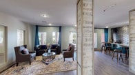 This thoughtfully designed leasing center offers a polished, single-floor layout that balances professional functionality with a warm, inviting atmosphere. Upon entry, visitors are greeted by a soaring vaulted ceiling and an arched doorway framing views of the outdoors, setting an impressive first impression. The main office area features a spacious work desk, modern art pieces on sage-green walls, and wood-look flooring that flows seamlessly throughout the space.

Rustic, whitewashed wood columns and a sliding barn door add distinctive farmhouse-inspired character, creating visual interest while subtly dividing the space. The lounge area is generously proportioned, furnished with plush seating arrangements, layered area rugs, and large windows dressed in teal drapery that invite ample natural light.

A standout kitchenette and bar area is highlighted by a bold metallic subway tile accent wall paired with dark green cabinetry, a countertop sink, and a built-in wine refrigerator. Nearby high-top tables with industrial-style bar stools provide a casual gathering spot. The leasing center also features a private meeting area accessed through the barn door, complete with comfortable seating and mirrored wall details. Overall, the space projects a modern yet approachable aesthetic ideal for welcoming prospective residents.