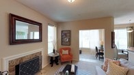 This single-story residence offers a thoughtfully designed layout across one bedroom and one bathroom. The living room serves as the heart of the home, featuring a tile-surround fireplace with a decorative hearth, neutral-toned walls, and a textured ceiling. Carpeting in the main living area adds warmth underfoot, while large windows allow generous natural light to fill the space. A wall-mounted mirror near the fireplace enhances the sense of openness.

Adjacent to the living room, a separate dining area is visible through an open doorway, benefiting from its own window that brings in additional daylight. The space accommodates a dining table and chairs comfortably, making it suitable for everyday meals or entertaining.

The overall color palette throughout is warm and neutral, creating a cohesive and inviting atmosphere. The open sightlines between the living and dining areas contribute to a connected, airy feel despite the intimate scale of the home. This single-level layout offers practical, comfortable living with key features like the fireplace and multi-room configuration providing added character and functionality.