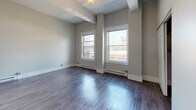 Located at 50 Franklin Street in the heart of Worcester, Massachusetts, this single-floor unit offers a thoughtfully designed layout with a clean, modern aesthetic throughout. The open living area is immediately inviting, showcasing rich hardwood-style flooring and neutral gray walls that create a bright, versatile backdrop. Large double-hung windows flood the space with natural light and frame views of the surrounding downtown Worcester cityscape, adding a strong sense of urban connection to the interior. Baseboard heating runs along the perimeter, ensuring year-round comfort.

The kitchen is a functional and stylish highlight, featuring dark charcoal cabinetry, granite-look countertops, a white subway tile backsplash with decorative accent tiles, and stainless steel appliances — all complemented by warm wood-tone flooring that ties the space together.

The bedroom offers generous proportions with hardwood-style floors, high ceilings with exposed structural elements that add character, and a built-in open closet providing practical storage. The bathroom includes a full tub-and-shower combination with white tile surround accented by bold color tiles, a vanity with medicine cabinet, and warm tile flooring. This unit combines functional living with a polished urban character in a prime downtown location.
