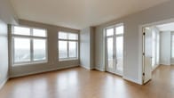This single-floor unit is characterized by a clean, contemporary design with neutral grey walls, warm hardwood-style flooring, and white trim that runs consistently throughout the space. The open-concept living and dining area is generously proportioned, benefiting from an abundance of natural light through large windows and glass-paneled French doors that lead to a private balcony offering elevated city views. The seamless indoor-outdoor connection enhances the sense of openness throughout the main living space.

The kitchen is designed for functionality and style, featuring dark espresso cabinetry that extends to the ceiling, stainless steel appliances including a refrigerator, range, and built-in microwave, a white subway tile backsplash, and a light-colored countertop island with an undermount sink. Recessed and pendant lighting adds a refined finish.

The bedrooms are well-lit with large windows framing city views and are finished with the same hardwood-style flooring. The bathrooms maintain the consistent design palette, with one featuring a full soaking tub and tiled surround, and another offering a dark vanity with a white countertop, framed mirror, and large-format tile flooring.