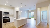 Located at 1001 Victory Lap Ln in Holly Ridge, NC, this well-appointed one-bedroom, one-bathroom home offers a thoughtfully designed single-level layout with a bright, modern aesthetic throughout. The open-concept kitchen and living area serves as the heart of the home, featuring light hardwood-style flooring, pendant lighting over a central island with a undermount sink, and a ceiling fan that keeps the space comfortable. The kitchen is outfitted with crisp white shaker cabinetry, a subtle tile backsplash, stainless steel appliances including a refrigerator, electric range, and microwave, and generous counter space. The living area receives natural light through a glass door that leads directly to an outdoor patio, offering a seamless indoor-outdoor connection. The bedroom is carpeted for comfort, fitted with a ceiling fan, and benefits from a bright window with neighborhood views and access to a dedicated closet. The bathroom features a white vanity with ample cabinetry, a framed mirror, modern lighting, and hardwood-style flooring. A dedicated laundry room houses a full-size washer and dryer with overhead wire shelving for added storage. The home's clean, neutral palette and modern finishes create a cohesive and inviting atmosphere throughout.