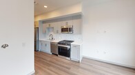 Located in Oxnard, California, this efficiently designed one-bedroom, one-bathroom unit offers a clean, modern aesthetic with quality finishes throughout its single floor. The layout is organized around a central hallway lined with recessed lighting, wood-look flooring, and gray-toned sliding barn doors with matte black hardware, creating a cohesive and contemporary look.

The kitchen is a standout feature, offering gray shaker-style cabinetry, white quartz countertops, a marble-look tile backsplash, and a full suite of stainless steel appliances including a gas range, dishwasher, microwave, and refrigerator. A stainless steel undermount sink with a matte black faucet completes the well-appointed space.

The bathroom is bright and clean, finished with light wood-look flooring, a full soaking tub with shower, built-in wall shelving, and a white vanity. The bedroom features soft carpeting, a ceiling fan, and a high horizontal window that allows natural light while maintaining privacy. A dedicated closet and in-unit laundry add practical convenience. The overall ambiance is fresh, modern, and move-in ready, ideal for those seeking a compact yet functional living space in Ventura County.