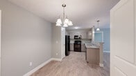 Located at 6712 Rivers Edge Cir in Utica, Indiana, this single-floor, 2-bedroom, 2-bathroom home offers a practical and modern layout designed for comfortable living. The open-concept kitchen and living area form the heart of the home, where light-toned hardwood-style flooring flows seamlessly throughout. The kitchen is well-equipped with gray shaker-style cabinetry, granite-look countertops, black appliances, and a peninsula with pendant lighting overhead — ideal for both meal prep and casual dining. An elegant multi-arm chandelier adds a refined touch to the dining area. The living room is bright and airy, featuring a ceiling fan and direct access to an exterior door with a glass panel, inviting natural light into the space. Both bedrooms are carpeted for warmth and comfort, each fitted with ceiling fans and ample room for furnishings. Three closets throughout the home offer generous storage options. The two bathrooms are finished with wood-look flooring, granite-topped vanities, and full tub-shower combinations with curtain rods. Neutral gray and taupe tones carried consistently across all rooms lend the home a cohesive, clean, and move-in-ready aesthetic.