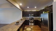 Located at 8254 County Rd 64 in Daphne, Alabama, this single-floor property offers a thoughtfully designed interior with standout finishes throughout. The kitchen is a focal point of the space, showcasing rich dark espresso cabinetry that extends to the ceiling and is accented by crown molding for an elegant touch. Granite-style countertops provide generous workspace, complemented by a double stainless steel sink. The kitchen is fully equipped with stainless steel appliances, including a smooth-top electric range, over-the-range microwave, and a full-size refrigerator. Recessed lighting illuminates the space warmly, highlighting the rich hardwood-style flooring underfoot. The U-shaped kitchen layout maximizes efficiency while offering an open, functional flow. Ample upper and lower cabinet storage ensures practicality without sacrificing style. The overall ambiance of the space is warm and inviting, with a cohesive dark-toned aesthetic balanced by neutral walls and warm lighting, creating a refined yet comfortable environment suited for both everyday living and entertaining.