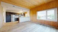 Located at 340 Dixwell Ave in New Haven, CT, this spacious 7-bedroom, 2-bathroom unit offers a distinctive architectural character defined by its signature use of natural wood. Tongue-and-groove wood paneling lines the walls and ceilings throughout much of the space, creating a warm, consistent aesthetic paired with light gray luxury vinyl plank flooring.

The open-plan living, dining, and kitchen area serves as the heart of the unit. The kitchen is outfitted with dark cabinetry, stainless steel appliances including a refrigerator and microwave, granite-style countertops, and a peninsula with pendant lighting overhead. A large window in the adjoining living area frames neighborhood rooftop views and fills the space with natural light.

The seven bedrooms vary in their finishes — several feature the warm wood-paneled walls and ceilings with windows offering exterior views, while others present clean white walls and the same plank flooring throughout. Each room provides a functional, well-proportioned layout.

The two bathrooms are finished with dark vanity cabinetry, white countertops, mirrored medicine cabinets, and vinyl plank flooring. A dedicated laundry area and two closets add practical utility. A hallway connects the various rooms, with clean white walls and light flooring maintaining a bright, cohesive flow throughout the unit.