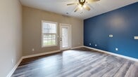 Located at 996 Coachman Drive in Richmond, Kentucky, this well-appointed one-bedroom, one-bathroom unit offers a thoughtfully designed single-floor layout. The open-concept kitchen and living area serves as the heart of the home, where white shaker-style cabinetry with matte black hardware pairs with granite countertops and a full suite of black stainless appliances, including a refrigerator, range, and over-the-range microwave. A pendant light fixture above the kitchen peninsula adds a modern touch, while wood-look luxury vinyl plank flooring runs consistently throughout the entire unit. The living room features a bold navy accent wall, a ceiling fan with light kit, and direct access to a private balcony overlooking the well-maintained grounds and surrounding community. The spacious bedroom receives ample natural light through dual windows and is equipped with its own ceiling fan. It provides direct access to a dedicated closet and connects conveniently to the full bathroom, which includes a tub/shower combo and matte black fixtures. A separate laundry area houses a full-size washer and dryer with overhead shelving. Neutral warm-gray tones throughout the unit create a clean, modern aesthetic that is both inviting and functional.