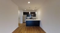 Located at 36 Pine St in Poughkeepsie, NY, this 2-bedroom, 2-bathroom residence offers a thoughtfully designed single-floor layout that balances modern aesthetics with everyday functionality. The open-concept kitchen and living area serves as the heart of the home, featuring rich hardwood-style flooring that adds warmth throughout the space. The kitchen is outfitted with dark cabinetry that contrasts sharply against light countertops, creating a sleek, contemporary look. A central island with an integrated sink provides additional workspace and casual seating potential, while stainless steel appliances — including a refrigerator, range, and built-in microwave — complete the professional-grade setup. Pendant lighting hangs above the island, complementing the recessed ceiling lights that illuminate the space evenly. A subway tile backsplash adds a clean, polished detail to the kitchen wall. The open flow between the kitchen and adjacent living area enhances the sense of spaciousness throughout. White walls and crisp trim maintain a bright, neutral backdrop that suits a variety of décor styles. With two bedrooms and two full bathrooms, this residence offers comfortable, well-appointed living in a modern setting.