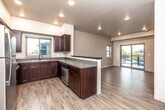 This single-floor unit offers a clean, contemporary design characterized by light wood-style flooring, neutral walls, and recessed lighting throughout. The open-concept layout connects the kitchen and living area seamlessly, creating a spacious and functional flow.

The kitchen is well-appointed with rich dark-stained cabinetry, stainless steel appliances including a refrigerator, range, microwave, and dishwasher, along with a double-basin sink and neutral countertops. A peninsula-style counter provides a natural divide between the kitchen and living space while maintaining the open feel. A window above the sink brings in natural light.

The living area is generously sized, featuring a sliding glass door that opens to a private balcony with views of the surrounding neighborhood. Additional bedrooms offer windows with exterior views, providing natural light and ventilation in each room.

The bathroom includes a vanity, toilet, and a shower-tub combination enclosed with glass sliding doors. A dedicated in-unit laundry room houses a full-sized washer and dryer with overhead wire shelving for added storage. Throughout the unit, the consistent flooring, neutral palette, and modern finishes contribute to a cohesive, contemporary ambiance.
