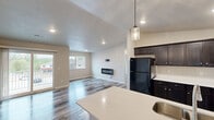 This thoughtfully laid-out single-floor residence features a seamless open-concept design connecting the kitchen, dining room, and living room into one cohesive, light-filled space. Durable wood-look flooring runs throughout, complementing the neutral warm-beige walls and clean white trim that define the home's modern aesthetic.

The kitchen is a standout feature, appointed with rich dark cabinetry, light quartz countertops, a stainless steel undermount sink, pendant lighting, and a full suite of appliances including an electric range and black refrigerator. An extended breakfast bar creates a natural divide between the kitchen and dining area.

The living room is bright and functional, featuring a wall-mounted electric fireplace and recessed lighting. A sliding glass door opens directly onto a private balcony, filling the room with natural light and offering views of the surrounding neighborhood.

The bedroom is a comfortable, well-proportioned retreat with a ceiling fan, a window with outdoor views, and wood-look flooring. It connects to a dedicated laundry room equipped with a full-size washer and dryer and wire shelving for storage.

The full bathroom features a combined tub and shower, dark vanity cabinetry with a white countertop, and wood-look tile flooring. Additional spaces include a hallway and utility room, rounding out a complete and practical floor plan.