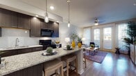 This well-designed single-floor residence offers a cohesive blend of modern style and functional living. The open-concept kitchen is a standout feature, showcasing rich dark cabinetry, granite countertops, a tile backsplash, and black stainless appliances. A large kitchen island with bar seating and elegant pendant lighting serves as both a prep space and a casual dining hub, flowing seamlessly into the living area.

The living room is bright and inviting, bathed in natural light from floor-to-ceiling glass doors that open to an outdoor area. Hardwood-style flooring, a ceiling fan, and generous wall space give the room a comfortable, airy feel.

The bedroom is a serene retreat, featuring plush carpeting, a ceiling fan, and a large window that allows ample natural light. The room provides a calm, neutral palette that promotes rest and relaxation.

The bathroom is finished with granite countertops, an undermount sink with brushed nickel fixtures, and a shower-tub combination with tile surround and a curved curtain rod, all complemented by dark cabinetry for a polished look.

Throughout the space, consistent design choices—granite surfaces, dark wood tones, and neutral wall colors—create a harmonious and sophisticated living environment.
