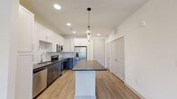 Located at 4000 Dr Walter S Davis Blvd in Nashville, TN, this well-designed one-bedroom, one-bathroom unit offers a thoughtful layout across a single floor. The open-concept living area seamlessly connects the kitchen, dining, and living spaces, creating an airy and functional environment. The kitchen is a standout feature, boasting a large center island with a dark countertop, two-tone cabinetry with white upper cabinets and gray lower cabinets, subway tile backsplash, and a full suite of stainless steel appliances including a refrigerator with ice maker, range, microwave, and dishwasher. Stylish pendant lighting illuminates the island, adding a modern touch. Light wood-style flooring flows throughout the main living areas, while recessed lighting keeps the space bright and welcoming. Natural light enters through sliding glass doors at the rear of the living area. The bedroom is comfortably proportioned, featuring plush carpet, a ceiling fan, and dual windows that bring in natural light. The bathroom includes a full soaking tub and shower combination with white tile surround, complemented by a vanity with a dark countertop. Additional utility rooms provide practical storage and laundry solutions, rounding out this efficiently designed Nashville residence.