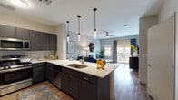 This single-floor residence is thoughtfully designed with an open-concept layout that seamlessly connects the kitchen, dining, and living areas. The kitchen is a standout feature, equipped with dark charcoal cabinetry, white quartz countertops, a mosaic tile backsplash, and a full suite of stainless steel appliances including a gas range, microwave, and French door refrigerator. A peninsula with an undermount sink and pendant lighting above provides casual seating and additional prep space, while wood-look flooring extends throughout the main living areas.

The living room offers a welcoming atmosphere with a ceiling fan, soft neutral walls accented by a muted blue feature wall, and access to a private balcony through glass doors, allowing natural light to fill the space. The bedroom is carpeted for comfort and features a ceiling fan, natural light from a window with striped curtains, and a spacious walk-in closet outfitted with a full rod-and-shelf system. The bathroom is finished with marble-style tile in the glass-enclosed shower, dark cabinetry with a white countertop vanity, and wood-look tile flooring, creating a clean, contemporary aesthetic throughout.