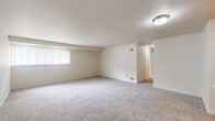 This single-floor residence offers a well-organized layout designed for comfortable everyday living. The generous living area is finished with plush wall-to-wall carpeting and neutral-toned walls, creating a bright and open atmosphere. A large window with vertical blinds allows natural light to fill the space, while a flush-mount ceiling light provides additional illumination.

The galley-style kitchen is efficiently arranged with warm wood cabinetry lining both sides, offering ample upper and lower storage. White appliances — including a coil-top range, refrigerator, and dishwasher — complement the light countertops, while wood-look vinyl flooring adds a clean, practical finish underfoot.

The bedrooms are carpeted and finished in soft neutral tones, each featuring windows with blinds that bring in natural light. The primary bedroom includes direct access to an en-suite bathroom and a closet nearby. The en-suite bathroom features a vanity with wood cabinetry, a single-basin sink, and a tiled shower-tub combination. A second bathroom is also present, outfitted with a standalone tiled shower stall. Throughout the residence, the consistent use of light colors and clean finishes contributes to a cohesive, move-in-ready aesthetic.