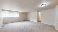 This single-floor residence offers a well-organized layout designed for comfortable everyday living. The generous living area is finished with plush wall-to-wall carpeting and neutral-toned walls, creating a bright and open atmosphere. A large window with vertical blinds allows natural light to fill the space, while a flush-mount ceiling light provides additional illumination.

The galley-style kitchen is efficiently arranged with warm wood cabinetry lining both sides, offering ample upper and lower storage. White appliances — including a coil-top range, refrigerator, and dishwasher — complement the light countertops, while wood-look vinyl flooring adds a clean, practical finish underfoot.

The bedrooms are carpeted and finished in soft neutral tones, each featuring windows with blinds that bring in natural light. The primary bedroom includes direct access to an en-suite bathroom and a closet nearby. The en-suite bathroom features a vanity with wood cabinetry, a single-basin sink, and a tiled shower-tub combination. A second bathroom is also present, outfitted with a standalone tiled shower stall. Throughout the residence, the consistent use of light colors and clean finishes contributes to a cohesive, move-in-ready aesthetic.