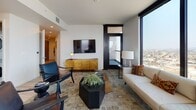Located at 1314 Franklin St in the heart of downtown Oakland, this single-floor residence sits high above the city, offering dramatic panoramic views of the Oakland skyline and surrounding hills through floor-to-ceiling windows and glass balcony doors. The open-concept living area is anchored by large-format windows that flood the space with natural light, creating a bright and airy atmosphere. The living room features light wood-style flooring, recessed lighting, and a wall-mounted television above a gold-toned media credenza, complemented by a mix of contemporary furnishings.

The modern kitchen is equipped with a substantial island topped with dark stone countertops, light wood cabinetry extending to the ceiling, stainless steel appliances, and a gas range, with a window framing additional city views. A light-filled hallway connects the living spaces to the bedrooms, with a decorative Oakland map adding a local touch.

Each bedroom benefits from expansive windows with commanding city views, light flooring, and ample natural light. The bathrooms are finished with clean, neutral tilework, including a glass-enclosed walk-in shower in the primary bath and a streamlined vanity in the secondary bath, maintaining a cohesive, contemporary aesthetic throughout.