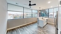 Located on the third floor at 1230 Elm St in downtown Manchester, NH, this thoughtfully designed unit offers a contemporary living experience with a well-organized layout across a single floor. The open-concept living and kitchen area is the heart of the space, anchored by a sleek kitchen island with a quartz countertop, undermount sink, and white cabinetry. Floor-to-ceiling windows line the exterior wall, flooding the area with natural light and offering sweeping views of the Manchester cityscape. A modern ceiling fan with a matte black finish adds both style and function to this bright, airy space. Wood-look plank flooring runs throughout the main living area, adding warmth and a clean aesthetic. Two well-proportioned bedrooms feature plush patterned carpeting, neutral gray walls, and large windows that continue the urban view. Each bedroom includes a dedicated closet with built-in shelving, providing ample storage. The full bathroom is finished with a tub-shower combination, matte black fixtures, wood-look tile flooring, a quartz vanity countertop, and a bright window overlooking the city below. Clean lines, modern finishes, and abundant natural light define the overall ambiance of this urban residence.