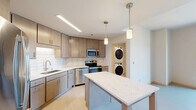 Located at 202 S Pinckney St in the heart of downtown Madison, Wisconsin, this modern one-bedroom, one-bathroom unit offers a thoughtfully designed layout with contemporary finishes throughout. The open kitchen is a standout feature, showcasing warm-toned flat-panel cabinetry, white quartz countertops, a subway tile backsplash, and a full suite of stainless steel appliances including a refrigerator, electric range, microwave, and dishwasher. A central island provides additional prep space and casual dining, all illuminated by pendant lighting overhead. Light-toned flooring flows seamlessly throughout the unit, creating a clean and cohesive aesthetic. The spacious bedroom offers natural light through tall vertical windows with expansive city views and features a ceiling fan for added comfort. A dedicated closet provides well-organized storage. The bathroom is finished in white tile with a full soaking tub and shower combination, brushed nickel fixtures, and recessed lighting for a clean, minimal look. A separate laundry room with stacked full-size washer and dryer units, along with built-in shelving, adds significant convenience. The unit combines functional design with modern finishes, making it an ideal residence in one of Madison's most vibrant downtown locations.