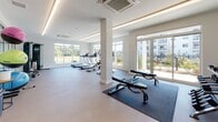 Located at 50 Perkins Farm Drive in Stonington, Connecticut, this single-floor fitness center is designed to support a comprehensive range of workout activities. The main exercise area is bright and spacious, featuring large floor-to-ceiling windows and glass doors that flood the space with natural light while offering views of the surrounding landscaped grounds and community. The clean, modern interior is finished with neutral-toned flooring, white walls, and structural columns that define workout zones without interrupting the open layout. Ceiling-mounted HVAC units and recessed linear lighting ensure consistent comfort throughout.

The cardio zone features a row of treadmills and elliptical machines positioned along the windowed perimeter, maximizing natural light during workouts. Strength training is supported by weight benches, a multi-functional cable machine, and an assortment of medicine balls displayed on a dedicated rack. Rowing machines add additional versatility to the equipment offerings.

A separate studio room provides a dedicated space for yoga, stretching, or group fitness classes. This room features soft blue-gray walls, a full wall of floor-to-ceiling mirrors, frosted windows for privacy, and smooth flooring ideal for mat-based workouts. Additional utility areas with white panel doors offer practical storage solutions, completing this thoughtfully appointed fitness facility.
