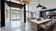The Henry's single-floor clubhouse and lobby area delivers a striking first impression through its dramatic architectural design. Soaring double-height ceilings define the main entry, accented by rich exposed wood beams and expansive floor-to-ceiling windows that flood the interior with natural light while framing views of the surrounding outdoors. Polished concrete floors extend throughout, lending a sleek, modern foundation to the space.

The reception area features a distinctive wood-paneled desk set against warm-toned walls adorned with sculptural metallic artwork, complemented by tall planters housing lush greenery. Adjacent seating areas are thoughtfully arranged, including a lounge with navy and amber upholstered chairs positioned near glass entry doors, and a relaxed sitting area with a textured sofa, layered area rug, and direct sightlines to a fitness center beyond glass partitions.

A built-in nook with cushioned bench seating and accent lighting provides an intimate retreat within the larger open layout. An island with a white quartz surface and pendant lighting anchors another social zone, while a dark-tiled accent wall adds depth and contrast. Throughout, a cohesive palette of navy, amber, wood tones, and white creates a sophisticated yet welcoming ambiance.