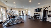 Located at 3511 Valley Rd in Bonita, this fitness center is a comprehensively outfitted single-floor facility designed to support a full range of workout routines. The space is divided into distinct functional zones, each thoughtfully arranged to maximize usability and flow.

The cardio area lines one side of the room and features multiple treadmills and elliptical machines, each equipped with individual monitors. Large French doors and windows along the walls flood this section with abundant natural light while offering views of an outdoor pool area, creating an inviting atmosphere for sustained cardio sessions.

The strength training zone is equally well-appointed, housing a multi-station cable machine, a flat weight bench, and a full rack of dumbbells spanning a wide range of weights. A wall-mounted flat-screen television overlooks this area. Rubber flooring throughout the entire space provides both safety and durability underfoot.

Architectural details include crown molding, recessed lighting, and textured ceilings, lending a polished, residential feel to the facility. Large mirrors on one wall enhance the sense of openness. A dedicated cycling area with a stationary bike rounds out the offerings. Access to the center is through glass-paneled French doors, maintaining a bright and open entry experience.